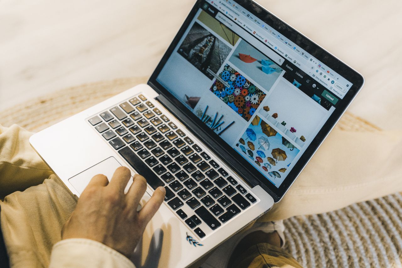 Une personne utilisant un ordinateur portable pour parcourir des sites de photos d’archives. Travail de freelance dans un cadre chaleureux.